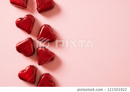 Romantic chocolate candy sweets as heart in red foil as frame on pink background. Valentine's day greeting card with copy space. View from above. Love concept. 121501922