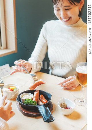 Two women eating sausages as a snack with craft beer 121502211