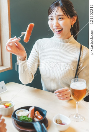 Two women eating sausages as a snack with craft beer 121502212