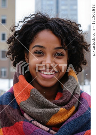 Vertical close up portrait of smiling African American woman wearing bright scarf standing outdoors in winter city and looking at camera 121502618
