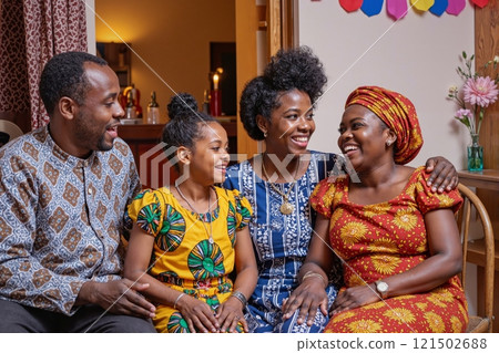 Portrait of happy African American family smiling sitting together and enjoying Kwanzaa celebration wearing colorful traditional outfits 121502688