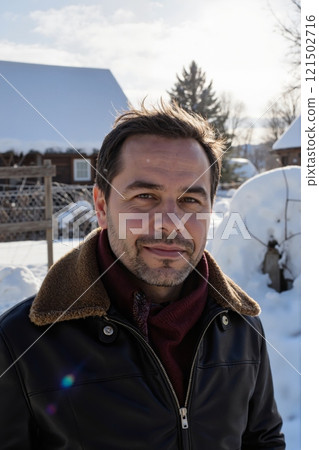 Vertical portrait of adult man looking at camera standing outdoors in winter with snow covered houses in background 121502716