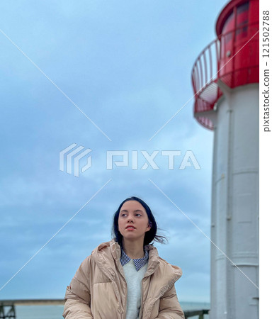 Woman standing on the wooden pier in front of the red lighthouse with blue sky and rainy clouds background in the Normandy, France. 121502788