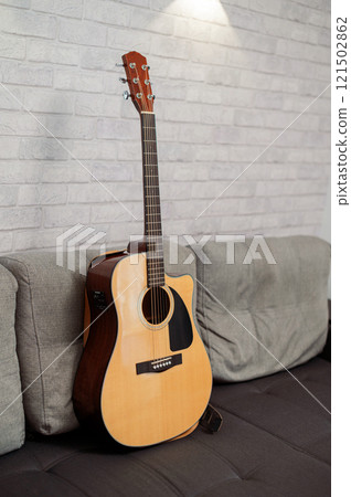 Beautiful six-string acoustic guitar, wood body, on sofa in studio Beautiful six-string acoustic guitar, wood body, on sofa in studio 121502862
