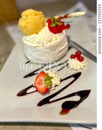 Meringue cake with cream and berries on a white plate with chocolate waves in a restaurant Meringue cake with cream and berries on a white plate with chocolate waves in a restaurant 121502914