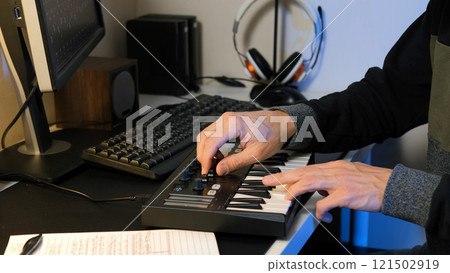 A man is immersed in composing a new music track using his MIDI keyboard controller in a home studio, capturing the creative process of crafting songs A man is immersed in composing a new music track using his MIDI keyboard controller in a home studio, capturing the creative process of crafting songs 121502919