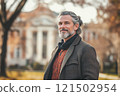 Waist up portrait of hip university professor with long hair looking at camera with academic buildings in background copy space 121502954