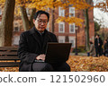 Waist up portrait of mature Asian professor working on laptop while sitting on bench in university campus surrounded by autumn trees copy space 121502960