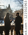 Vertical back view of two university professors chatting standing on balcony overlooking historic campus buildings under bright winter sunlight 121502963
