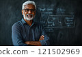 Waist up portrait of Indian man as senior professor wearing glasses and looking at camera confidently standing in front of blackboard copy space 121502969