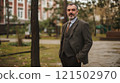 Waist up portrait of classic senior professor wearing tweed suit standing in green campus courtyard and looking at camera copy space 121502970