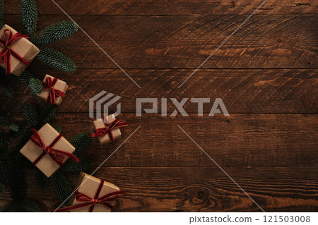 Christmas gifts in brown kraft paper with red velvet ribbons and sprigs of evergreen fir trees on a brown wooden background. Space for your text. 121503008