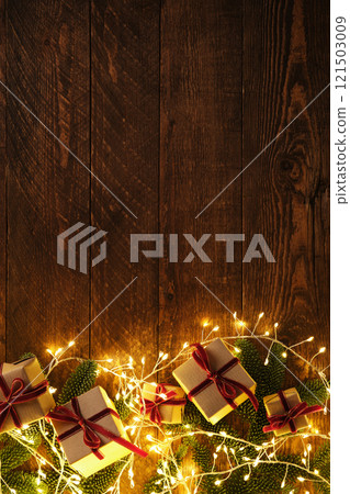 Vertical banner with brown kraft paper gifts with red velvet ribbons among sprigs of evergreen fir tree and garlands on brown wooden background. Space for your text. Vertical banner with brown kraft paper gifts with red velvet ribbons among sprigs of evergreen fir tree and garlands on brown wooden background. Space for your text. 121503009
