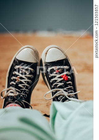 Black and white women's Converse sneakers with pink butterflies beads, woman relaxing on a sandy beach. Vacation by a sea in summer. Summertime travel 121503857