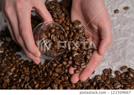 Woman's hands picks fresh aromatic roasted coffee beans into a small glass, craft paper background. Arabica and robusta blend Woman's hands picks fresh aromatic roasted coffee beans into a small glass, craft paper background. Arabica and robusta blend 121504667
