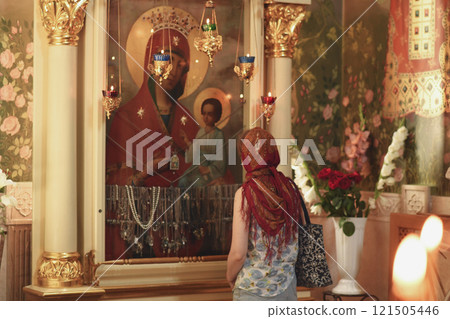 Russian woman in red headscarf praying near icon 121505446