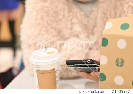 一位女士在室內開放式咖啡館一邊享用咖啡一邊操作智慧型手機 121505537