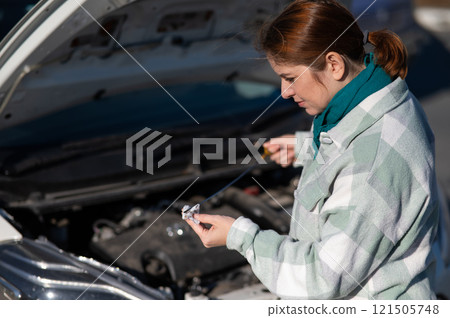 Caucasian female driver checking oil level in car engine.  121505748