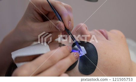 A woman undergoing eyelash extension procedure using an ultraviolet lamp. 121505753