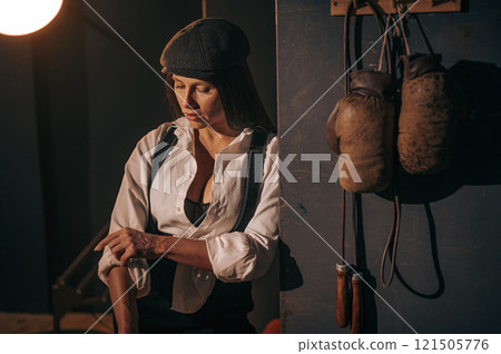 Caucasian woman in a Peaky Blinders style men's suit posing in a retro gym. 121505776