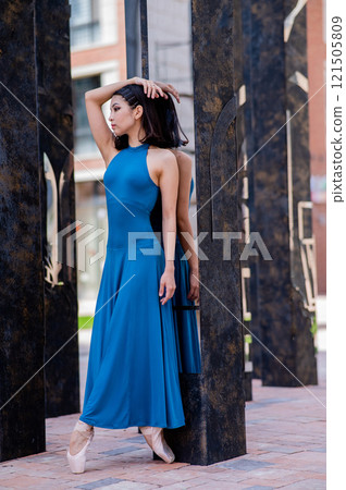 Beautiful asian ballerina in blue dress and pointe shoes posing outdoors. Vertical photo.  121505809