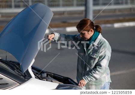 Caucasian female driver checking oil level in car engine.  121505859