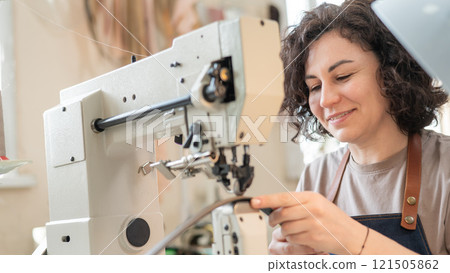 A woman tanner sews a leather belt on a sewing machine.  121505862