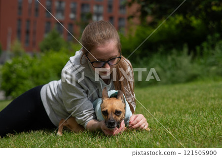 Young Caucasian woman lying on the lawn while walking with a small dog.  121505900