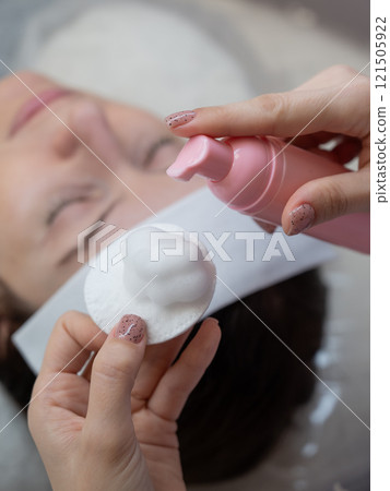 A professional applies cleansing foam to a cotton pad in a beauty salon. A professional applies cleansing foam to a cotton pad in a beauty salon. 121505922