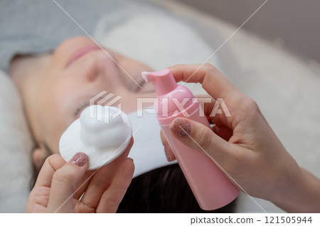 A professional applies cleansing foam to a cotton pad in a beauty salon.  121505944
