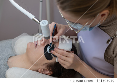 A woman undergoing eyelash extension procedure using an ultraviolet lamp. A woman undergoing eyelash extension procedure using an ultraviolet lamp. 121505949
