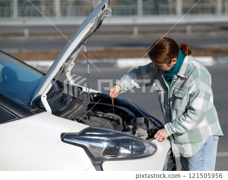 Caucasian female driver checking oil level in car engine.  121505956