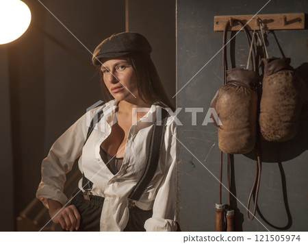 Caucasian woman in a Peaky Blinders style men's suit posing in a retro gym. 121505974