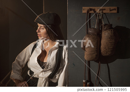 Caucasian woman in a Peaky Blinders style men's suit posing in a retro gym. Caucasian woman in a Peaky Blinders style men's suit posing in a retro gym. 121505995