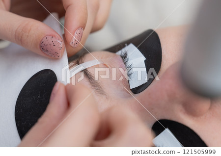 A specialist glues a client's drooping eyelid before eyelash extensions. A specialist glues a client's drooping eyelid before eyelash extensions. 121505999