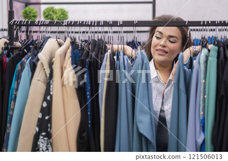 A smiling fat woman in a plus size store chooses clothes while sorting through the hangers. A smiling fat woman in a plus size store chooses clothes while sorting through the hangers. 121506013