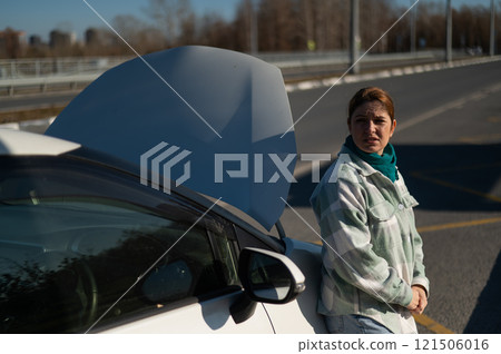 Sad Caucasian woman calling on phone while standing near car with open hood.  121506016