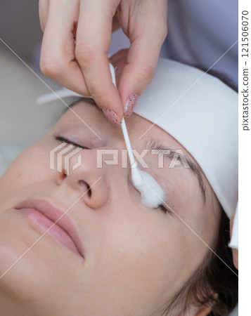 The master applies cleansing foam to the client's eyelashes using a cotton swab. The master applies cleansing foam to the client's eyelashes using a cotton swab. 121506070
