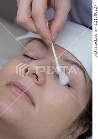 The master applies cleansing foam to the client's eyelashes using a cotton swab. The master applies cleansing foam to the client's eyelashes using a cotton swab. 121506127