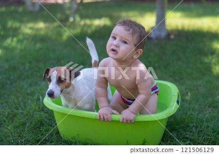 Cute boy bathes in a basin with a Jack Russell terrier dog outdoors in the summer. 121506129