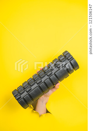 Female hand sticking out with MFR roller from yellow paper background. Vertical photo.  121506147