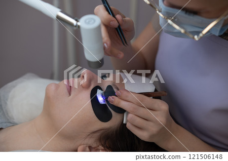 A woman undergoing eyelash extension procedure using an ultraviolet lamp. A woman undergoing eyelash extension procedure using an ultraviolet lamp. 121506148