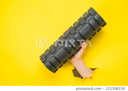 Female hand sticking out with MFR roller from yellow paper background. 121506150