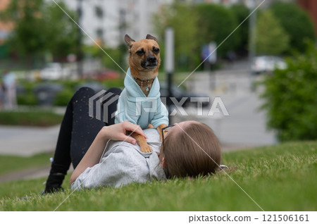 Young Caucasian woman lying on the lawn while walking with a small dog.  121506161