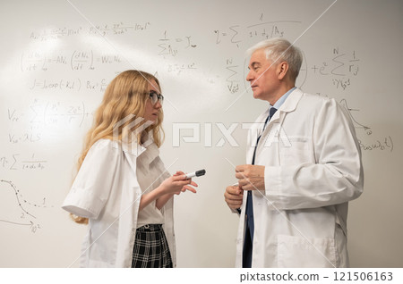 An elderly man and a young woman at a white board. Colleagues scientists discuss work issues. An elderly man and a young woman at a white board. Colleagues scientists discuss work issues. 121506163
