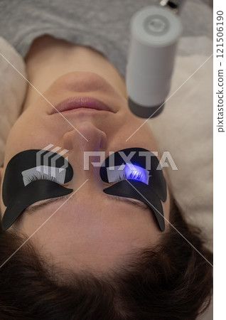 A woman undergoing eyelash extension procedure using an ultraviolet lamp. 121506190