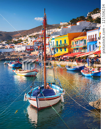 A picturesque harbor scene with colorful fishing boats and buildings in the background, under a bright blue sky 121506234