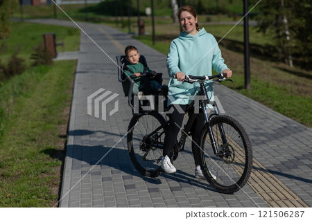 Caucasian woman riding a bicycle with her toddler son sitting behind her in a child seat. Caucasian woman riding a bicycle with her toddler son sitting behind her in a child seat. 121506287