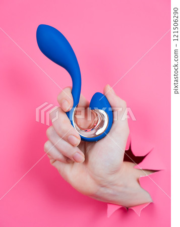 Hand with blue vibrator sticking out through pink paper background. Vertical photo.  121506290