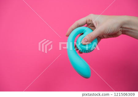 Woman holding blue curved sex toy on pink background. Copy space. Woman holding blue curved sex toy on pink background. Copy space. 121506309